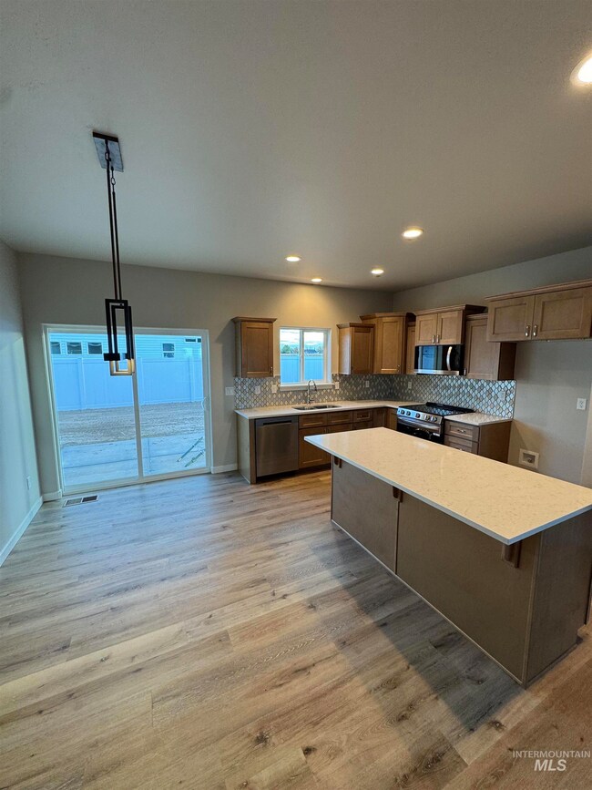 Kitchen with backsplash, decorative light fixtures, light wood-style floors, a kitchen island, and recessed lighting