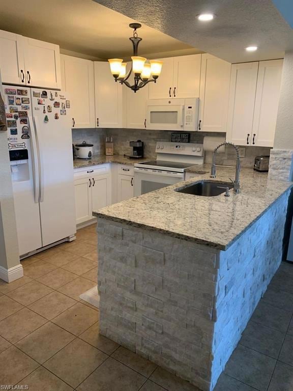 Kitchen featuring white appliances, white cabinets, light stone counters, a peninsula, and light tile patterned floors