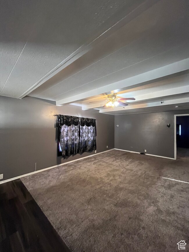 Spare room featuring beam ceiling, ceiling fan, dark carpet, and a textured ceiling