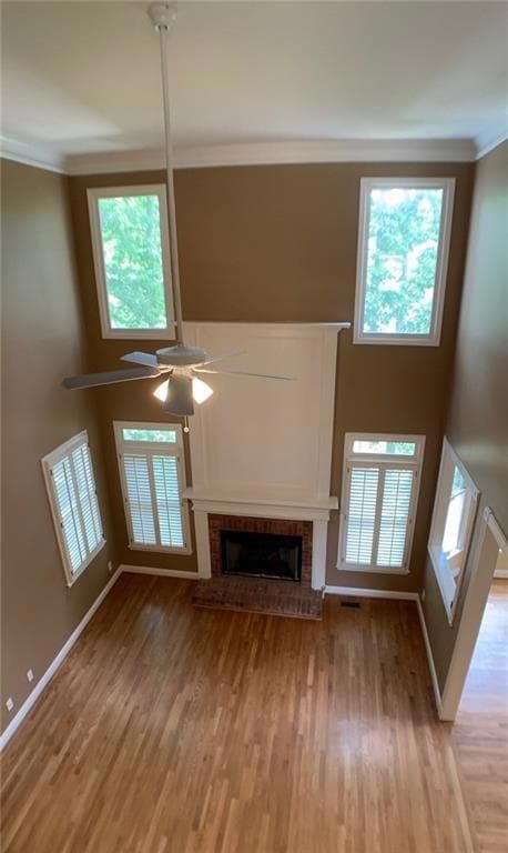 Unfurnished living room with a high ceiling, crown molding, a fireplace, light wood-type flooring, and a ceiling fan