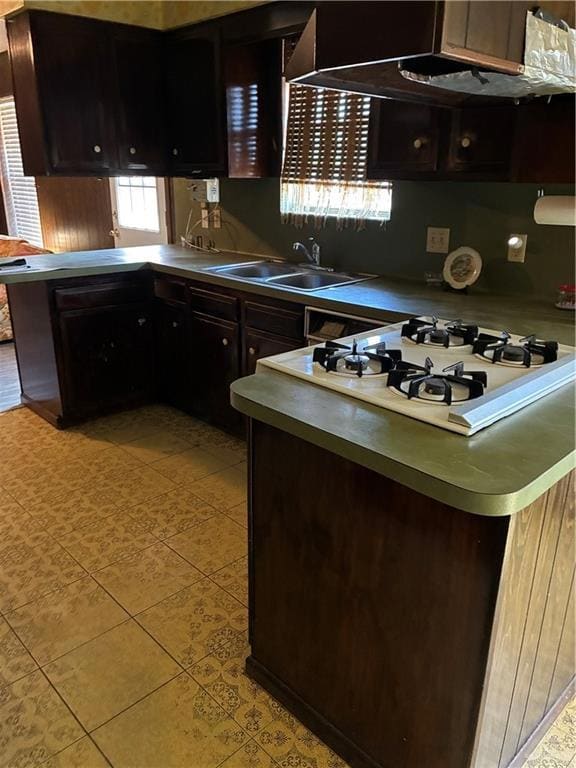 Kitchen with a peninsula, ventilation hood, dark brown cabinets, stovetop, and light countertops