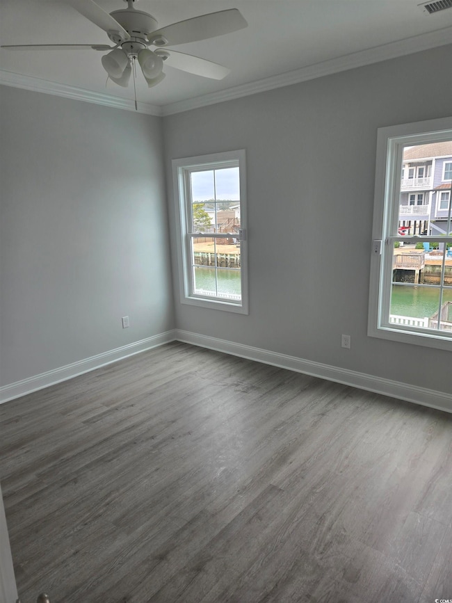 Empty room featuring crown molding, dark wood-style flooring, baseboards, and a ceiling fan