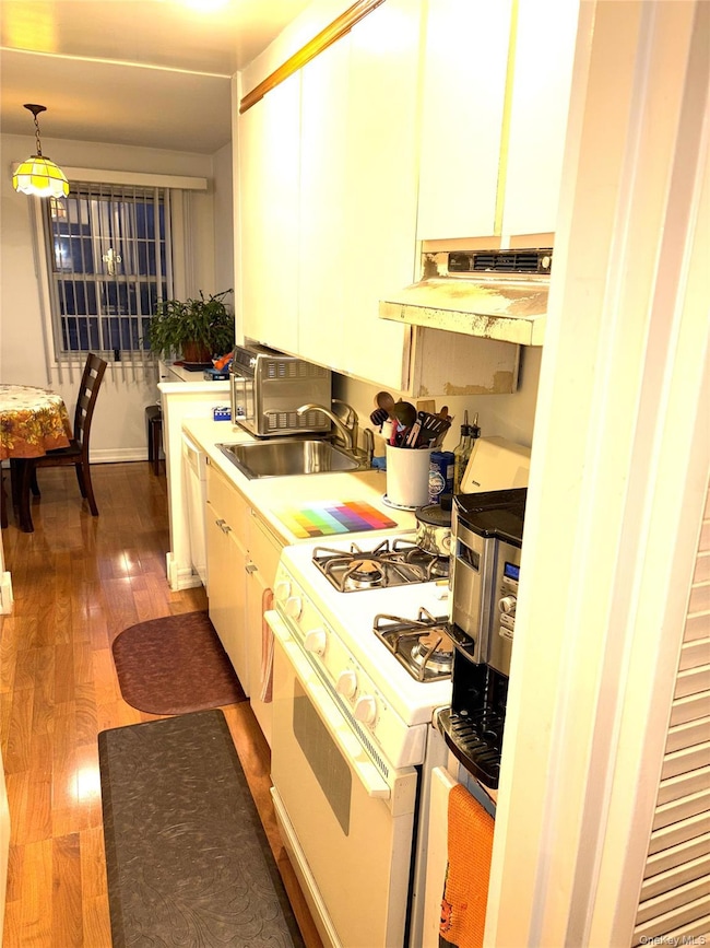 Kitchen with gas range gas stove, light countertops, hanging light fixtures, ventilation hood, and dark wood finished floors
