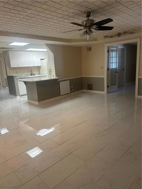 Unfurnished living room featuring a ceiling fan, light marble finish floors, and wainscoting