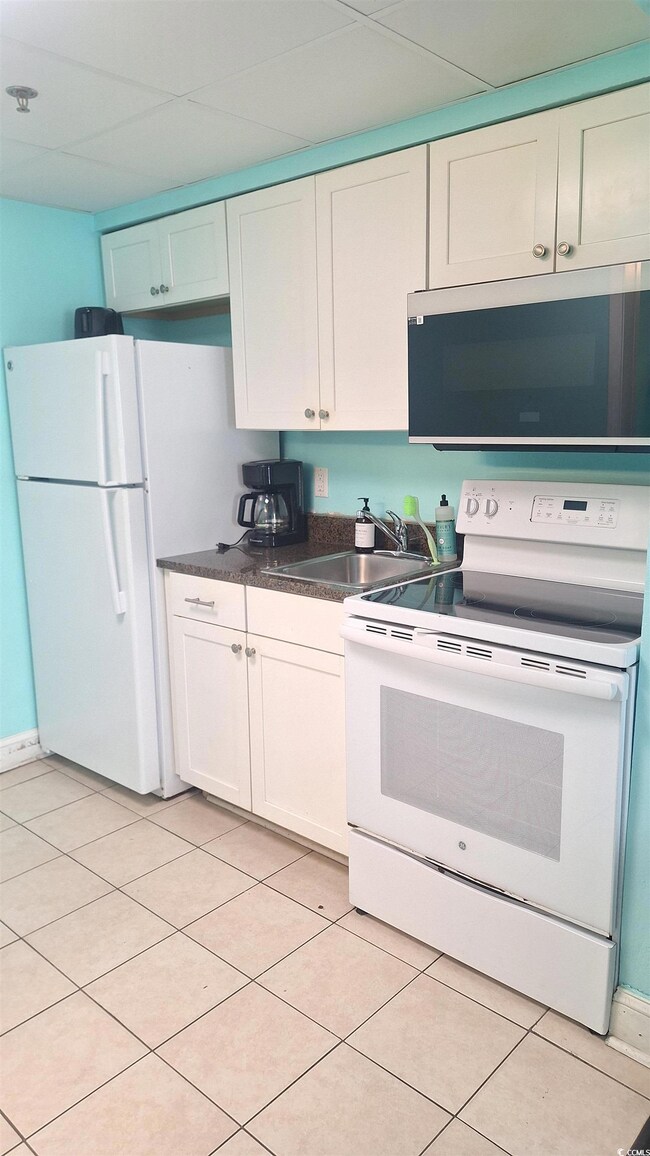 Kitchen with white appliances, dark countertops, white cabinets, and light tile patterned floors