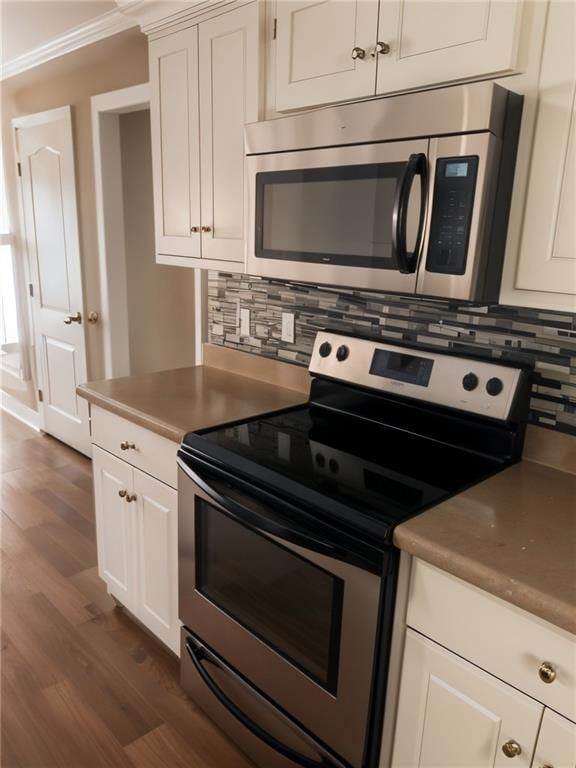 Kitchen with stainless steel appliances, dark wood-style floors, decorative backsplash, white cabinetry, and ornamental molding