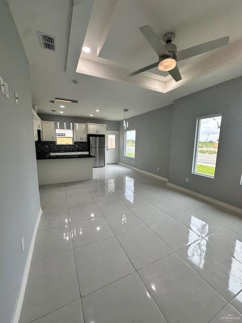 Unfurnished living room featuring a raised ceiling, light tile patterned floors, ceiling fan, and recessed lighting