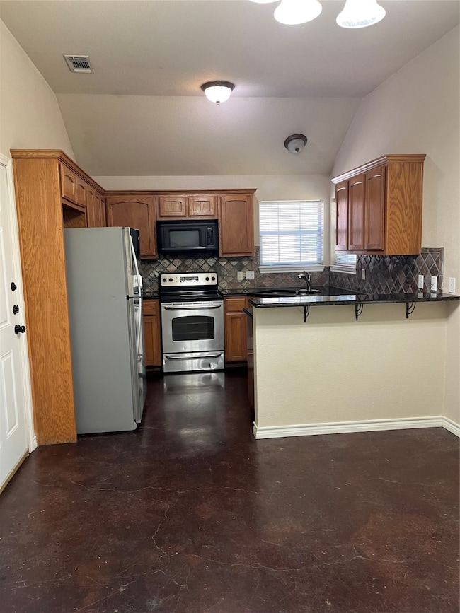 Kitchen with lofted ceiling, brown cabinetry, tasteful backsplash, fridge, and stainless steel range