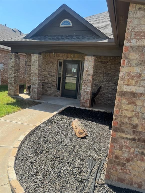 View of exterior entry featuring brick siding and roof with shingles