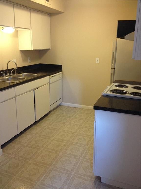 Kitchen featuring dark countertops, white cabinets, white appliances, and light floors