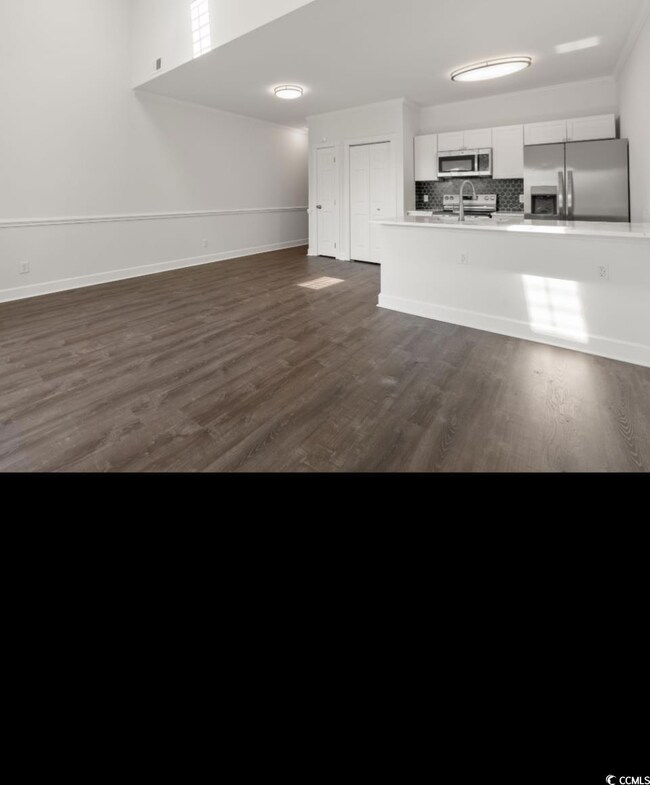 Unfurnished living room featuring dark wood-type flooring and baseboards
