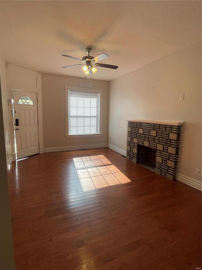 Unfurnished living room with hardwood / wood-style floors, a fireplace, a textured ceiling, and ceiling fan