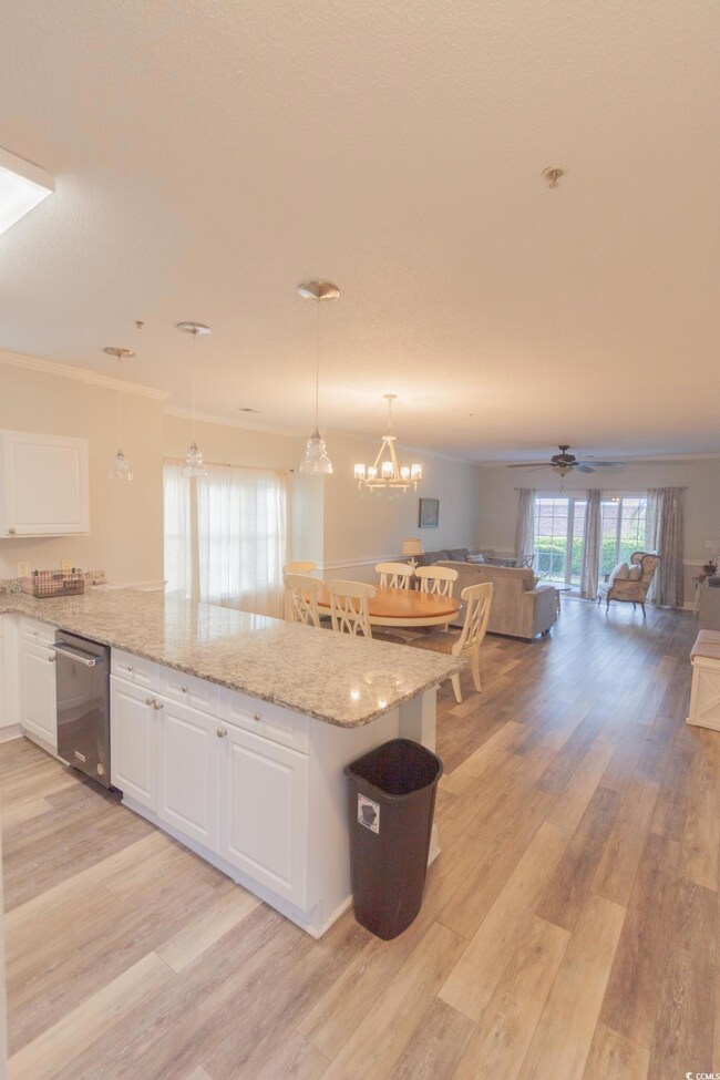 Kitchen with crown molding, white cabinetry, open floor plan, light stone counters, and light wood-type flooring