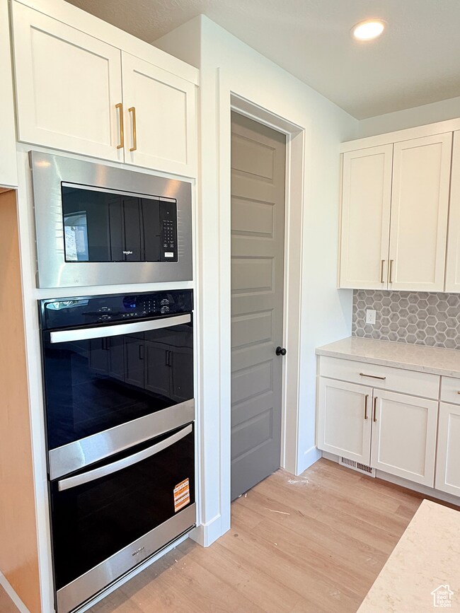 Kitchen featuring white cabinetry, appliances with stainless steel finishes, decorative backsplash, light wood-type flooring, and recessed lighting