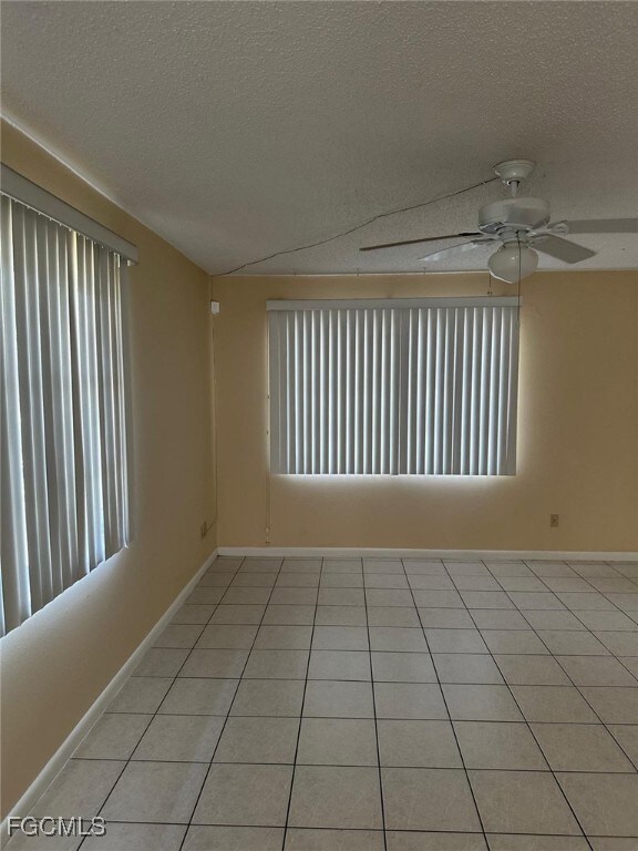 Unfurnished room with a textured ceiling, light tile patterned flooring, ceiling fan, and healthy amount of natural light
