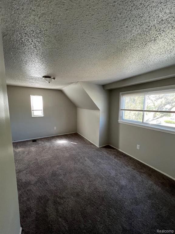 Bonus room featuring a textured ceiling, lofted ceiling, and dark colored carpet