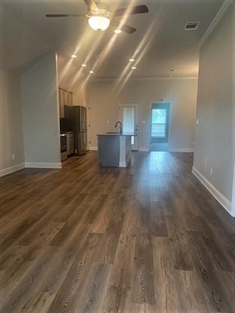 Unfurnished living room with a ceiling fan, crown molding, baseboards, a sink, and dark wood-style flooring