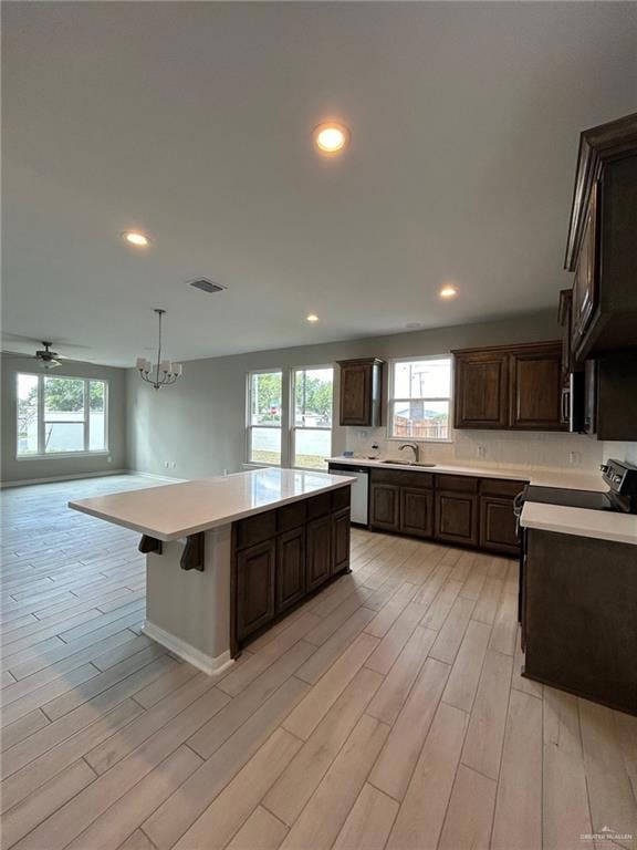 Kitchen with hanging light fixtures, dark brown cabinets, light wood-type flooring, recessed lighting, and a breakfast bar area