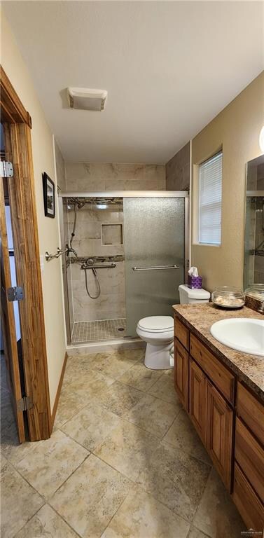 Bathroom featuring toilet, tile floors, a shower with shower door, and vanity