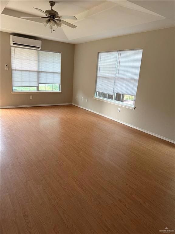 Unfurnished room featuring a wall unit AC, ceiling fan, wood finished floors, and baseboards