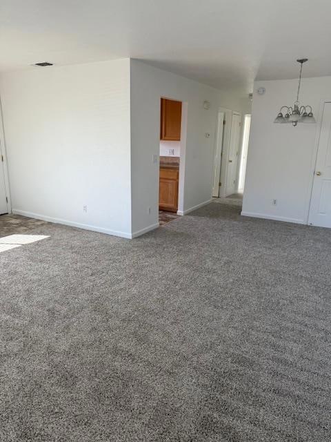unfurnished living room with carpet flooring and a chandelier