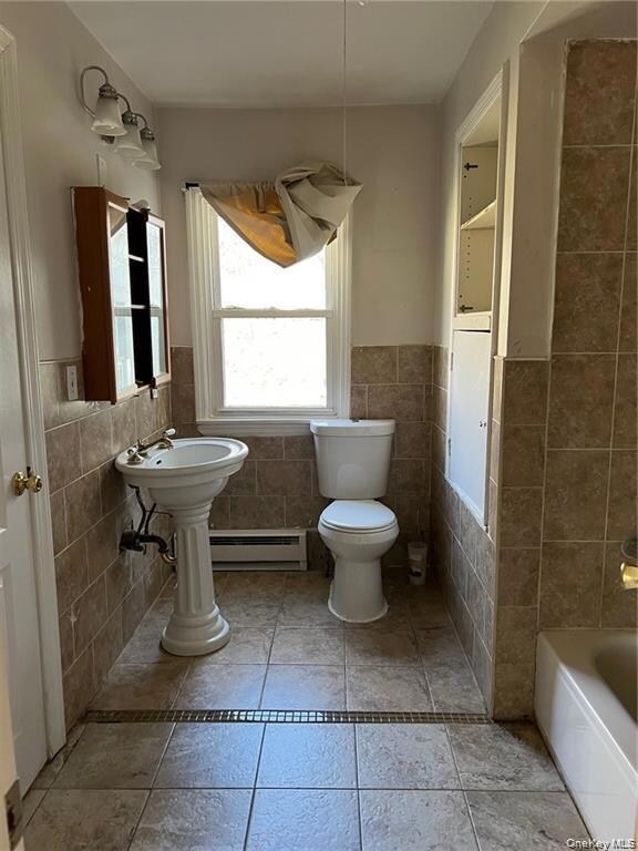 Bathroom featuring tile walls, a baseboard radiator, light tile patterned floors, and wainscoting