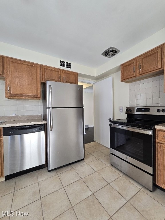 Kitchen with decorative backsplash, brown cabinets, appliances with stainless steel finishes, and light tile patterned flooring