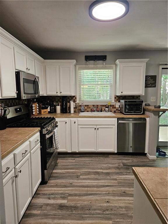 Kitchen with dishwashing machine, stove, backsplash, sink, and white cabinetry