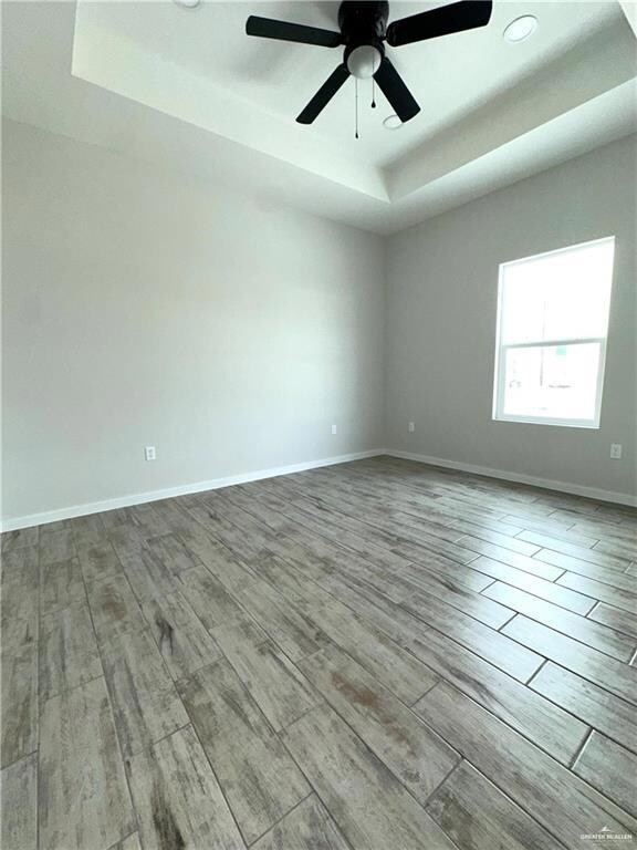 Spare room featuring a tray ceiling, light hardwood / wood-style flooring, and ceiling fan