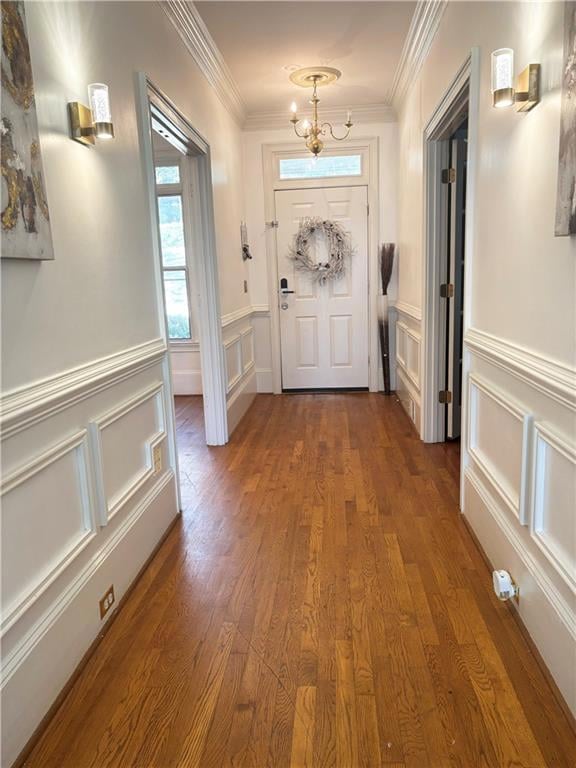 Doorway with a decorative wall, wood finished floors, ornamental molding, a chandelier, and a wainscoted wall