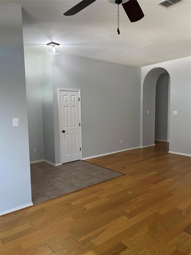 Empty room with a textured ceiling, wood-type flooring, and ceiling fan