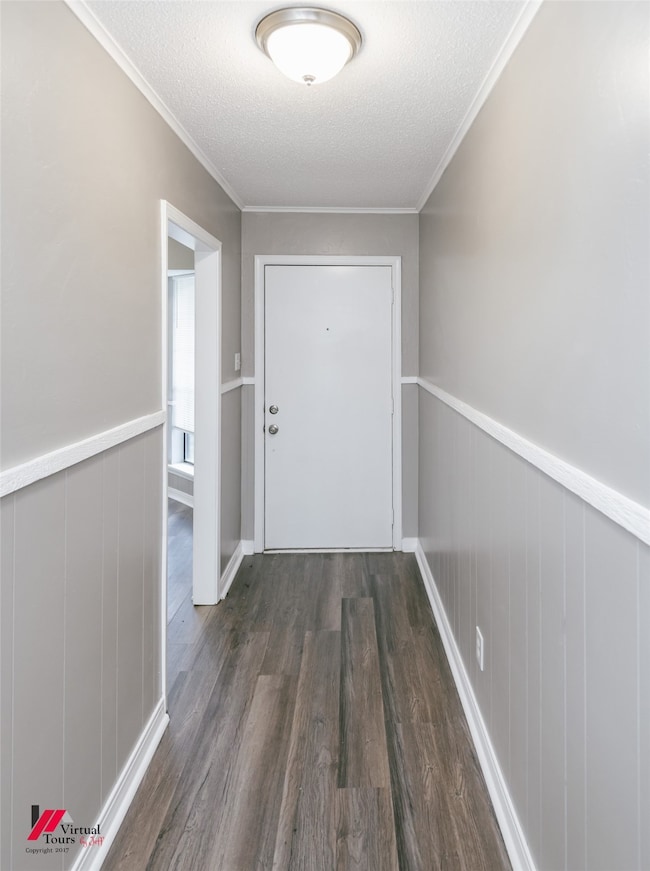 Entryway with a textured ceiling, a wainscoted wall, dark wood-style flooring, and crown molding