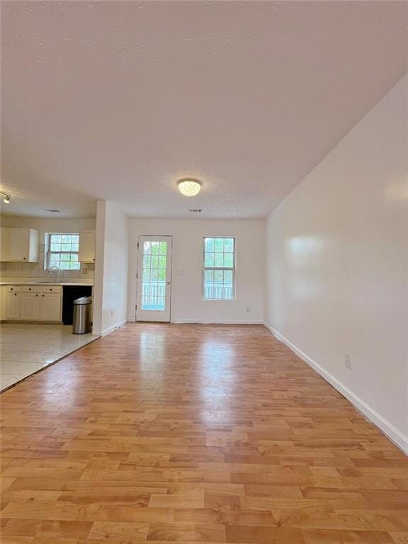 Unfurnished living room featuring light wood-style flooring, baseboards, and a sink