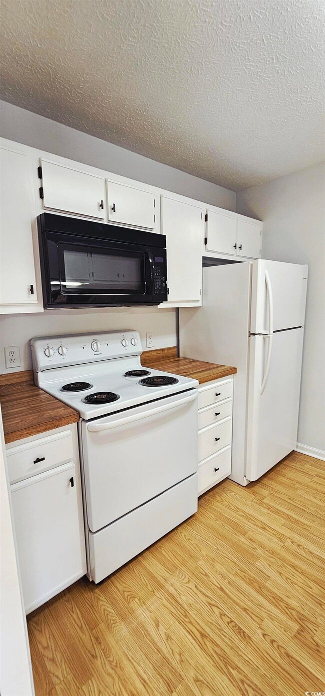 Kitchen with white appliances, white cabinets, light wood finished floors, and a textured ceiling