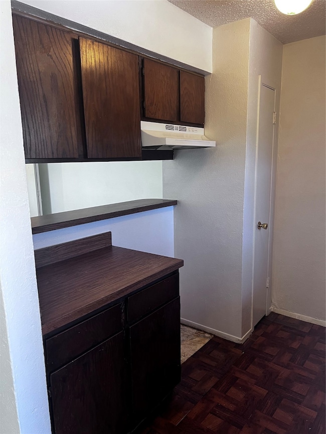 Kitchen with dark brown cabinetry, a textured ceiling, dark countertops, extractor fan, and a textured wall