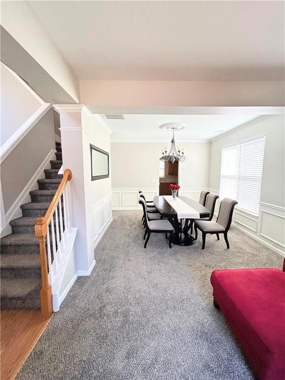 Dining space with stairs, ornamental molding, a decorative wall, a chandelier, and carpet flooring