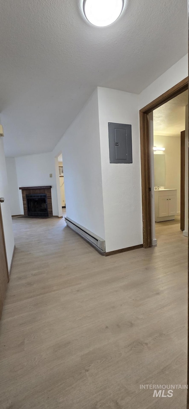 Corridor with a textured ceiling, electric panel, a baseboard radiator, and light wood-type flooring