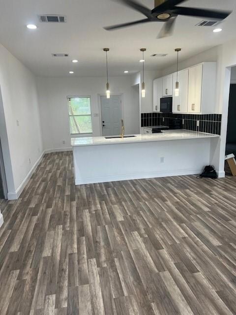 Kitchen featuring sink, kitchen peninsula, backsplash, dark hardwood / wood-style floors, and white cabinetry