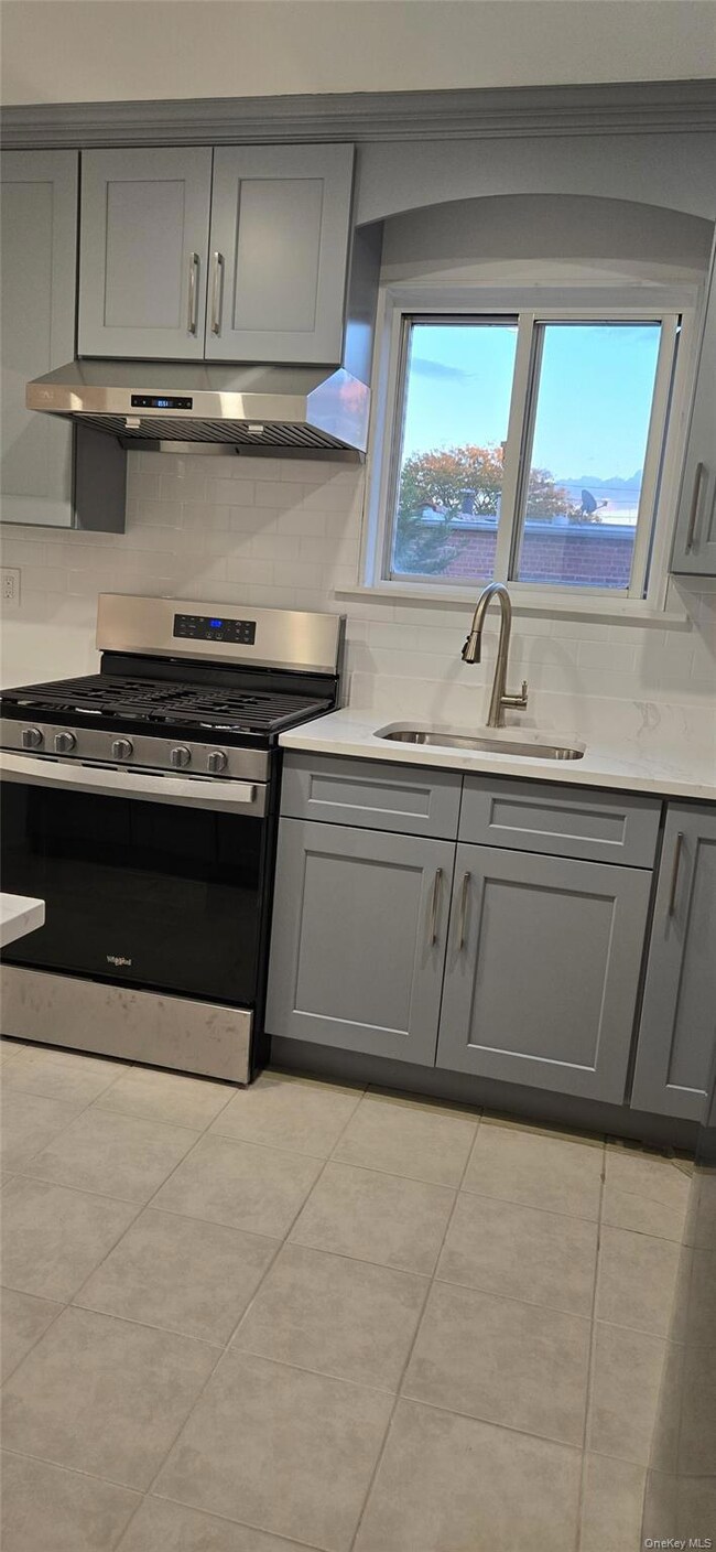 Kitchen featuring gray cabinets, stainless steel range with gas cooktop, backsplash, and under cabinet range hood