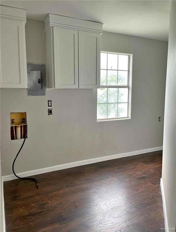 Laundry room with washer hookup, electric panel, baseboards, dark wood-style floors, and cabinet space