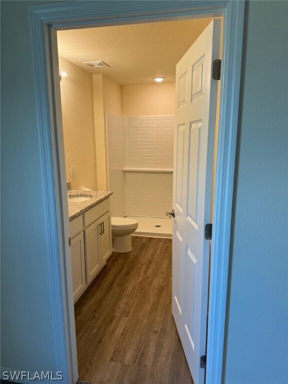 Bathroom with a shower, toilet, wood-type flooring, vanity, and a textured ceiling