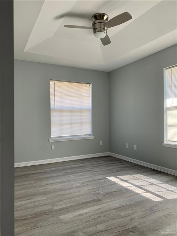 Unfurnished room featuring a raised ceiling, light wood-style flooring, and a ceiling fan
