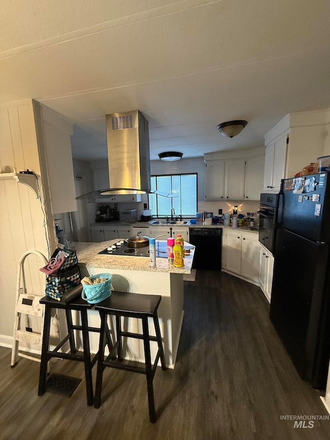 Kitchen with a peninsula, dark wood-style floors, island range hood, black appliances, and a breakfast bar
