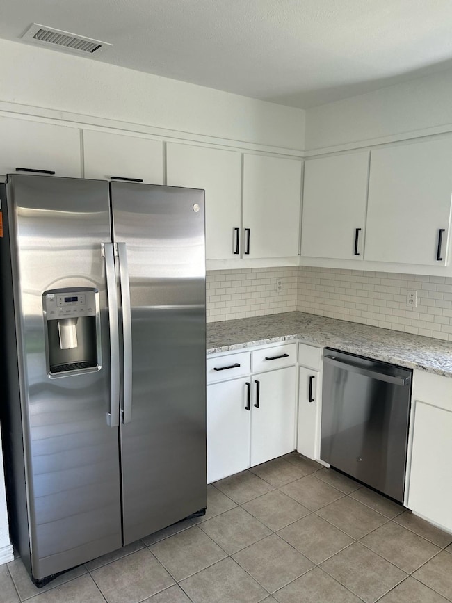 Kitchen featuring appliances with stainless steel finishes, tasteful backsplash, white cabinets, and light stone countertops