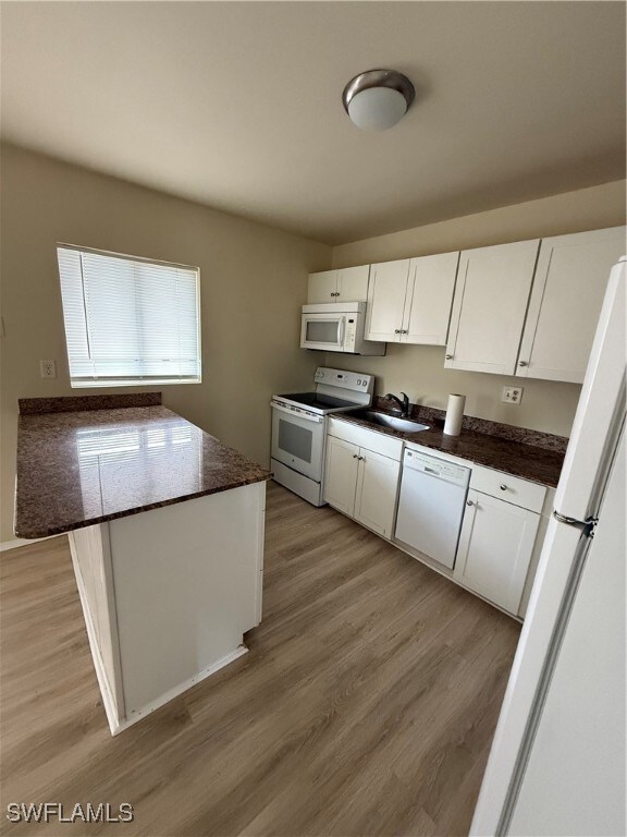 Kitchen featuring dark stone counters, white range with electric cooktop, light hardwood / wood-style flooring, dishwashing machine, and white cabinetry