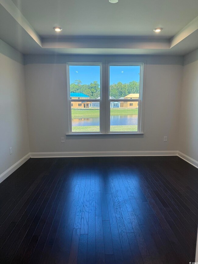 Empty room with a raised ceiling, dark wood-type flooring, a water view, and recessed lighting