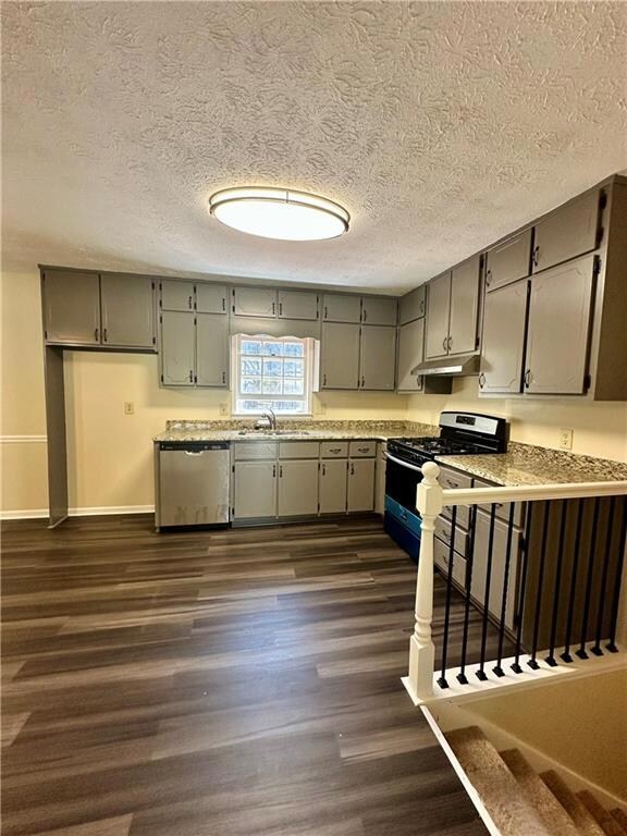 Kitchen featuring gray cabinetry, stainless steel appliances, a textured ceiling, dark wood finished floors, and under cabinet range hood