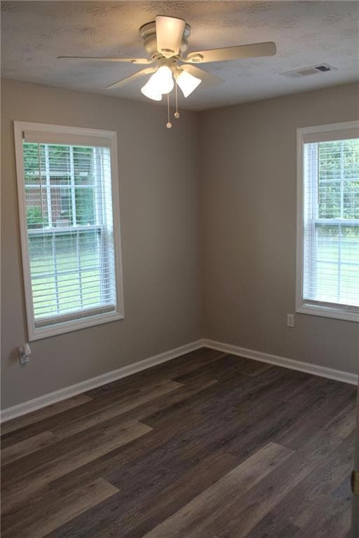Empty room featuring healthy amount of natural light, dark wood-style flooring, and ceiling fan
