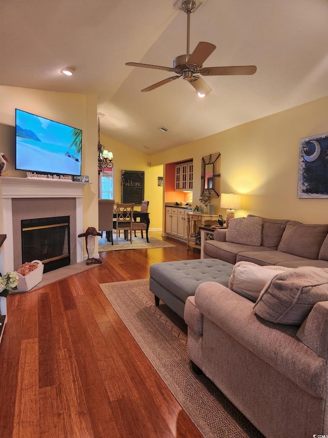 Living area featuring vaulted ceiling, wood finished floors, a tiled fireplace, ceiling fan, and recessed lighting