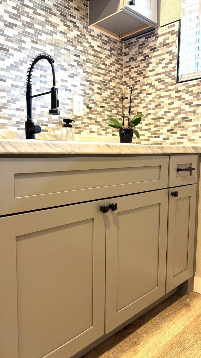 Kitchen featuring tasteful backsplash, light wood-style floors, gray cabinets, and light stone countertops